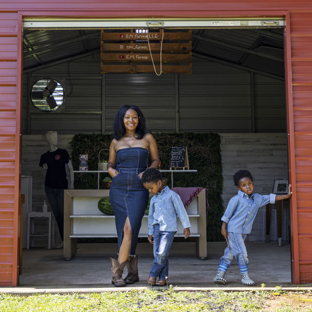 Twin boys standing with their mom in front of a red barn.